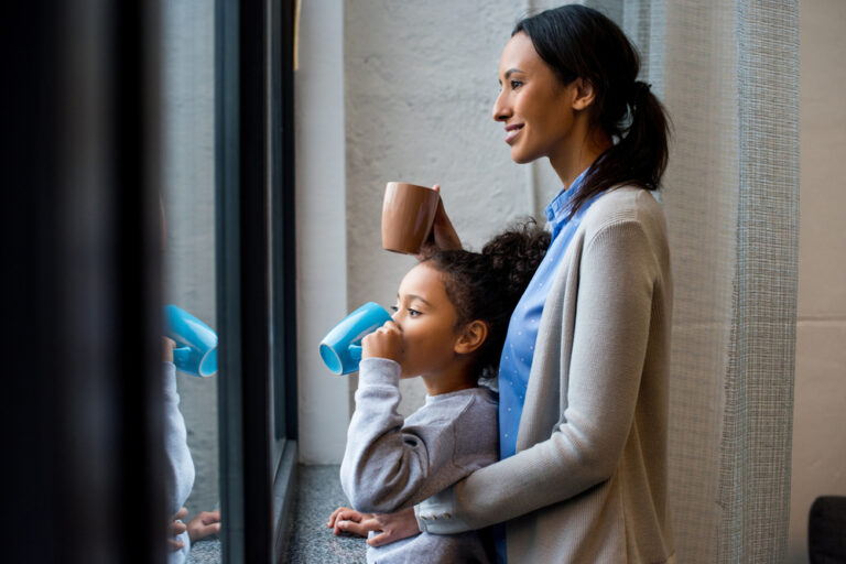 Mother and daughter drinking from coffee mugs by window