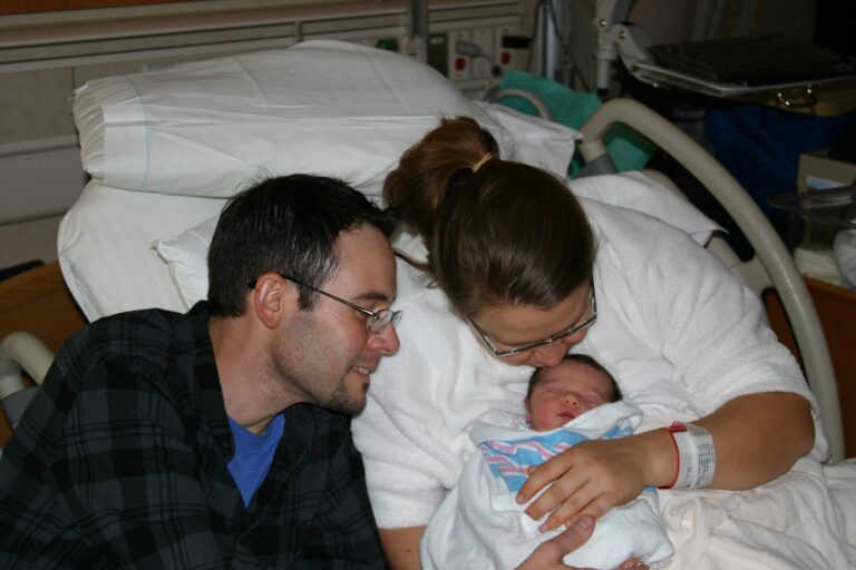 Husband and wife in hospital bed with newborn, color photo