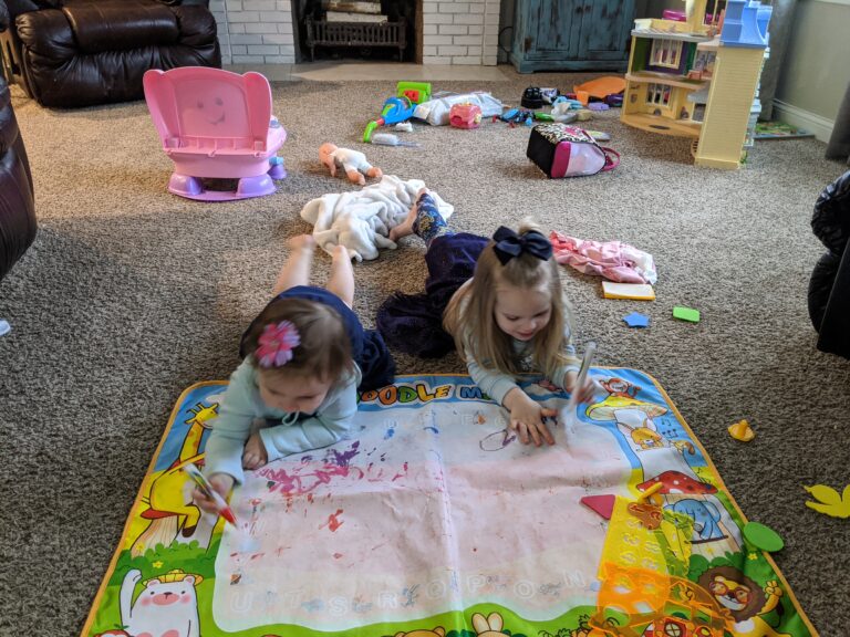 Two young girls lying on the floor with toys scattered, color photo