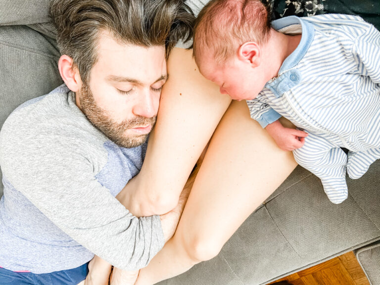 Newborn baby and father asleep on mother's legs at home