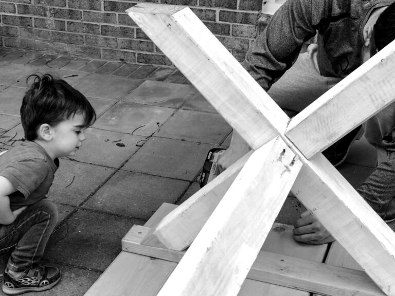 Little boy watching dad build something in backyard