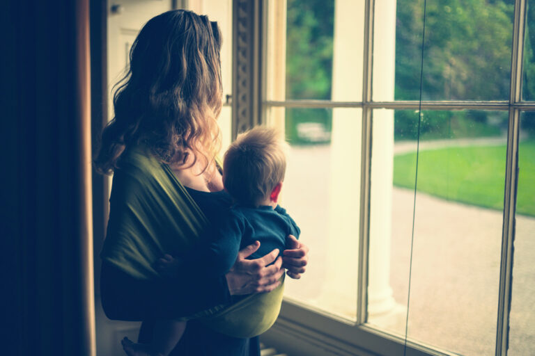 Woman holding toddler looking out front window at home