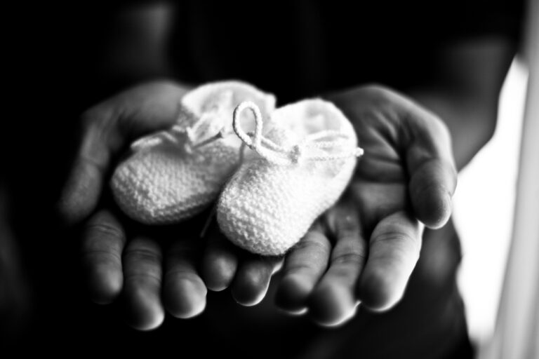Black and white hands holding baby booties