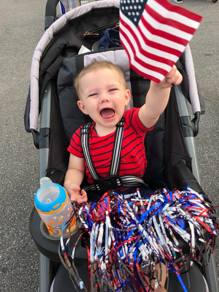 Baby in stroller holding an American flag, color photo
