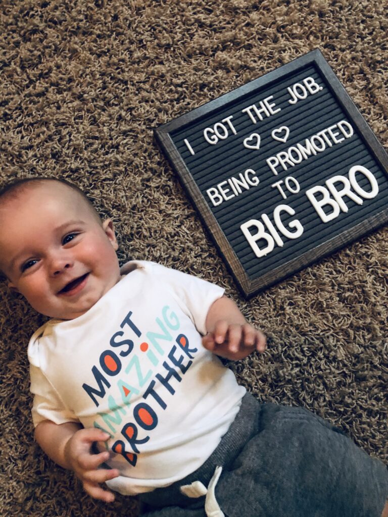 Baby boy next to pregnancy announcement sign, color photo
