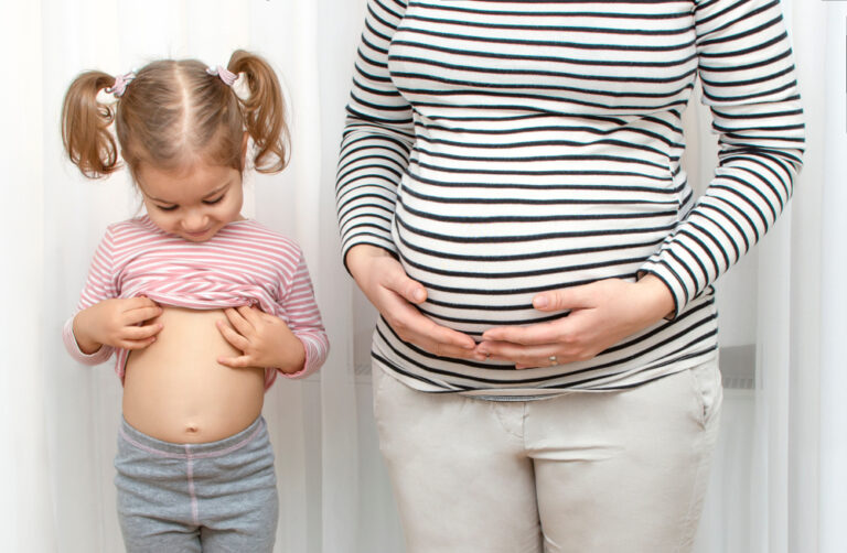 Little girl standing with pregnant mom looking at stomach