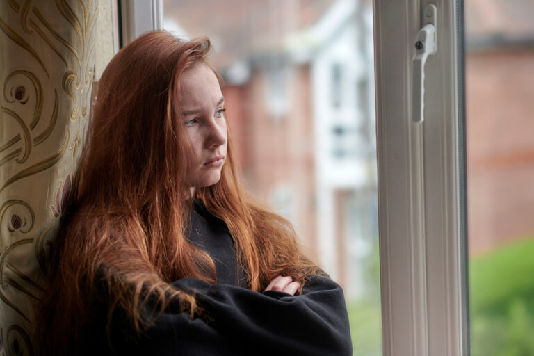 Teen girl looking out window with arms crossed
