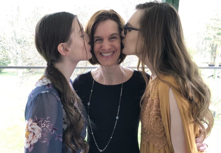 Two teen daughters kissing mother