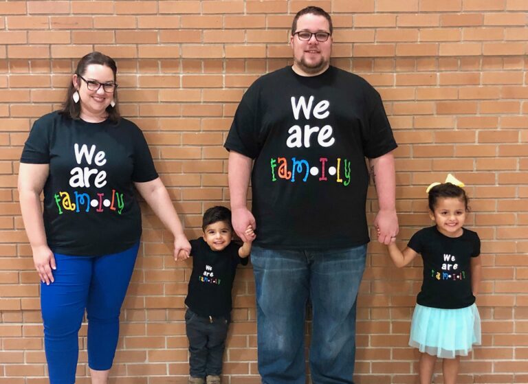 Husband, wife, two kids wearing We Are Family shirts, color photo