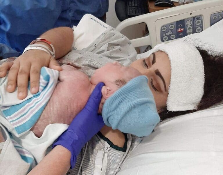 Woman holding newborn in hospital bed, color photo