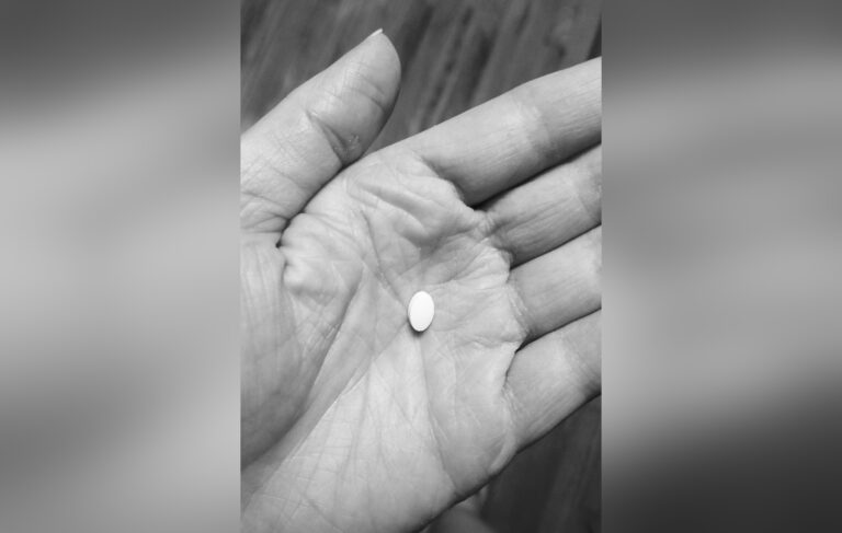Woman's hand with small, white pill, black-and-white photo