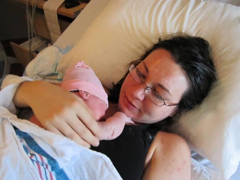 Woman holding newborn daughter in hospital bed, color photo