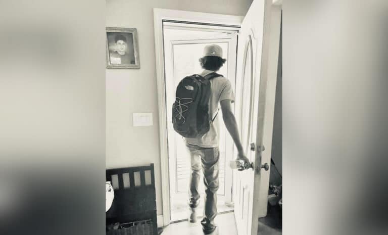 Teenage boy walking out the door with a backpack, black-and-white photo