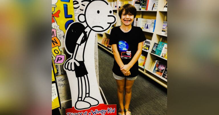 Young girl standing next to Diary of a Wimpy Kid cutout, color photo