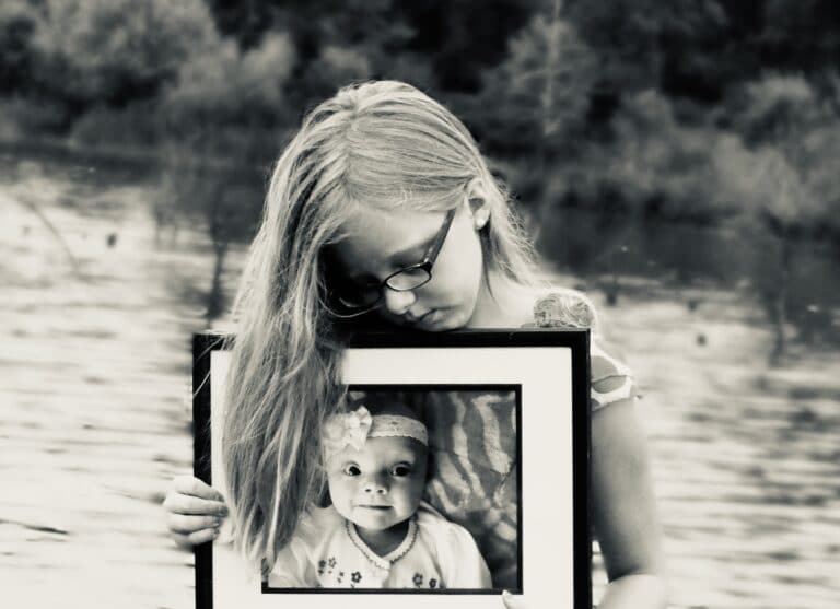Young girl holding photo of baby sister in frame, black-and-white photo