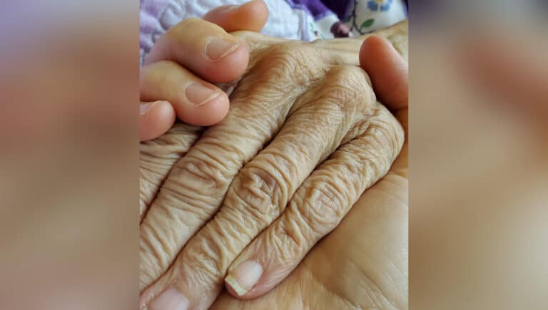 Woman holding mother's hand, color photo