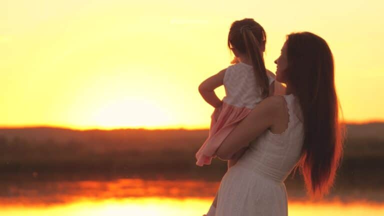 Mom holding child outside at sunset