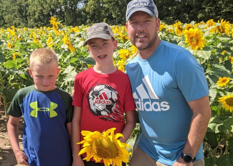 Father and two sons in sunflower field, color photo