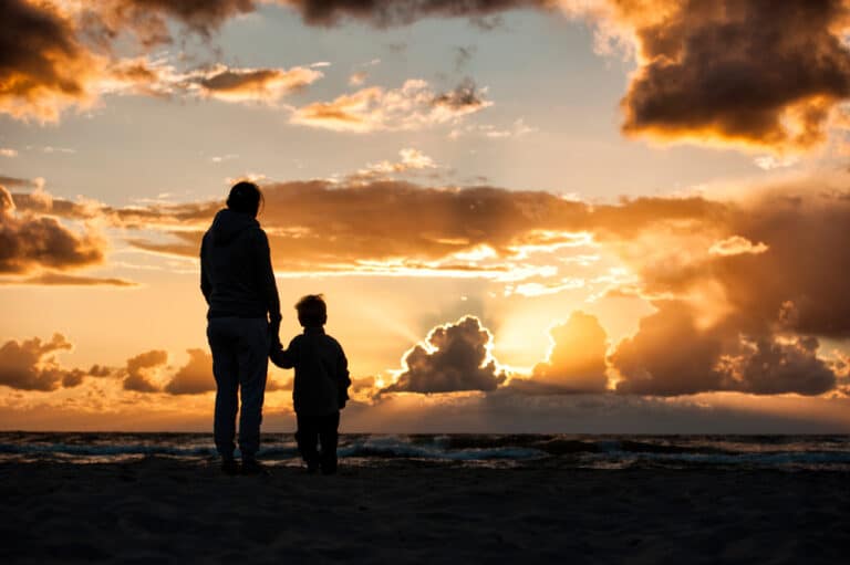 Woman holding child's hand at sunset