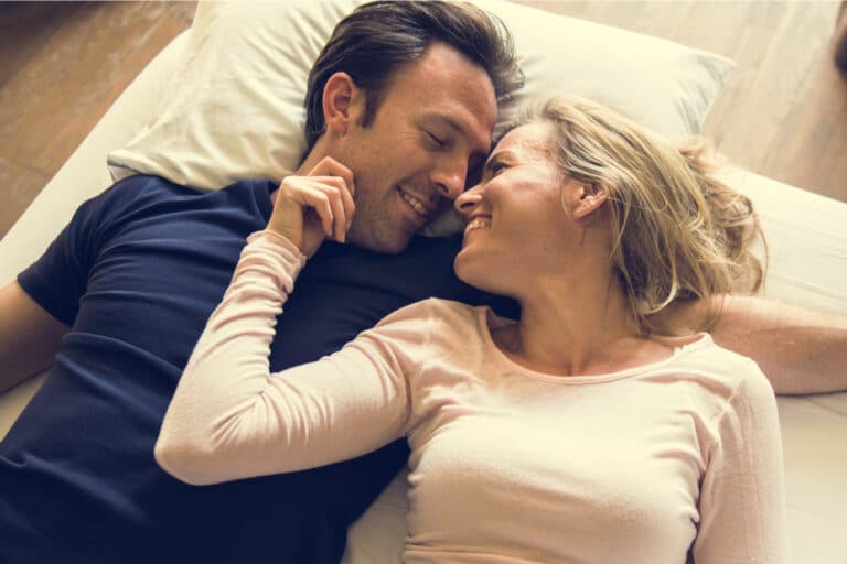 Man and woman snuggle on bed and smile