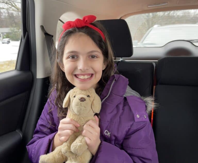 Girl sitting in car holding stuffed animal, color photo