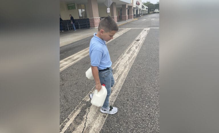 Young boy carrying two gallons of milk, color photo