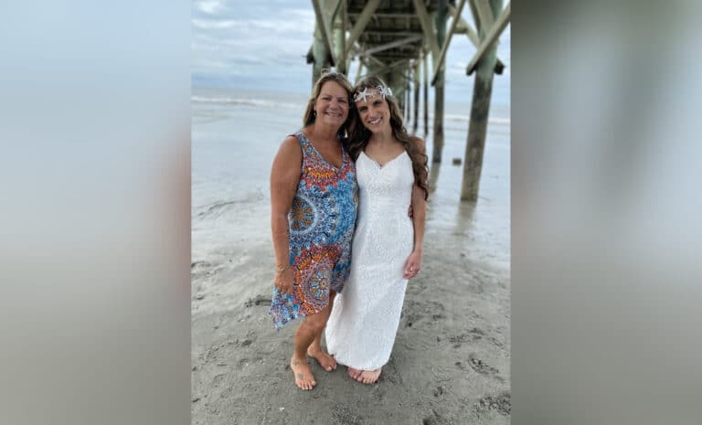 Mother with daughter in wedding dress on beach, color photo