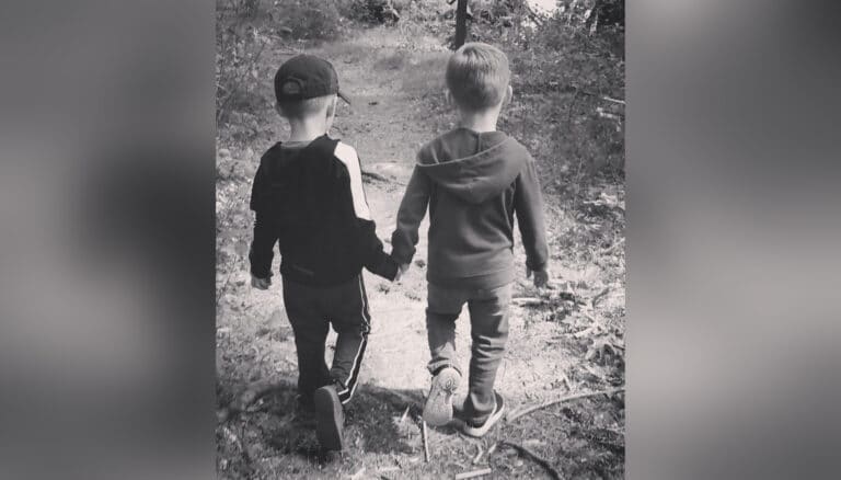 Twin boys walking along path holding hands, black-and-white photo