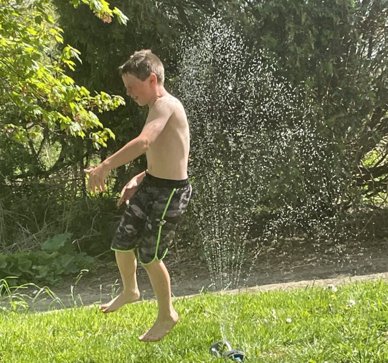 Boy jumping through sprinkler