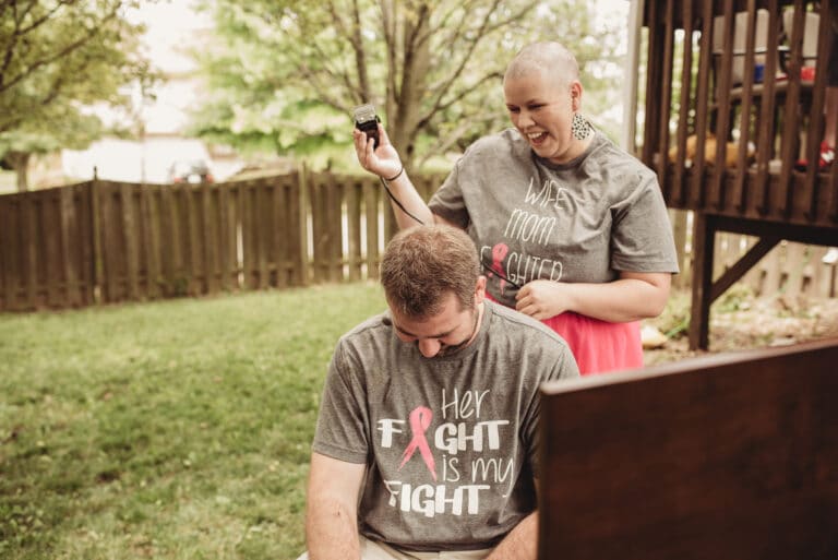 Bald woman holding clippers over husband's head, color photo