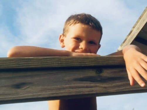Little boy peeking over wooden fence, color photo