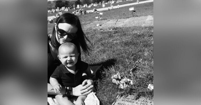 Mother holding baby near grave, black-and-white photo