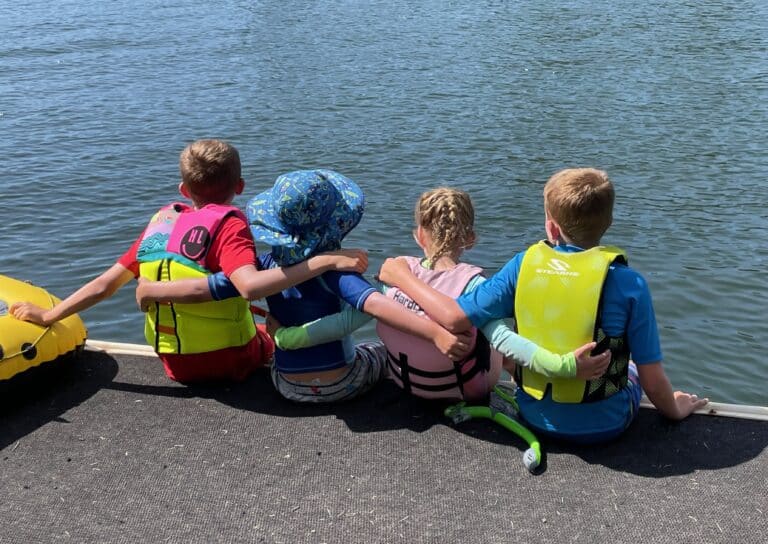Four kids sitting on the edge of a lake, color photo