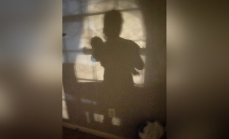 Shadow against a wall of woman holding a baby, color photo