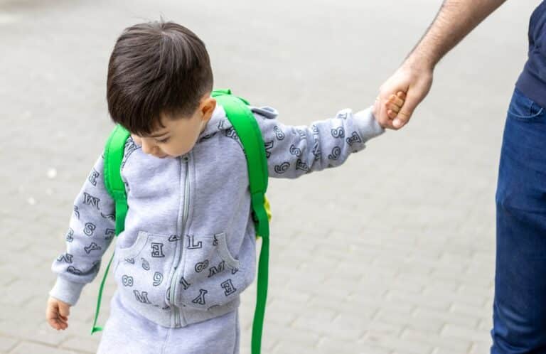 Little boy with green backpack holding man's hand