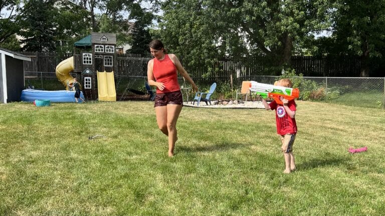 Mom running through sprinkler with child, color photo