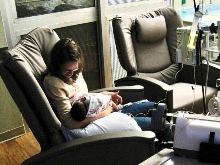 Woman smiling at newborn in hospital chair