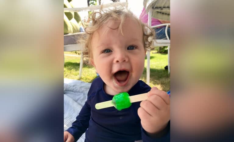 Toddler smiling and holding popsicle, color photo