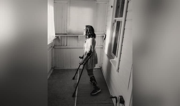 Woman with crutches looking out window, black-and-white photo