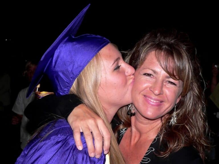 High school graduate kissing mother on cheek