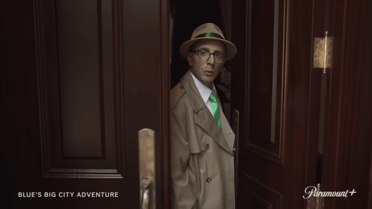 man in a trench coat and green tie looking out door