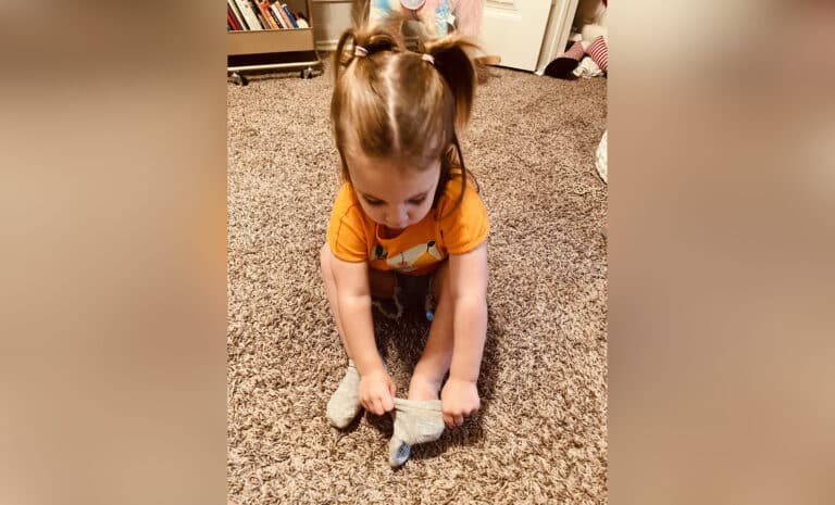 Toddler girl putting on sock, color photo