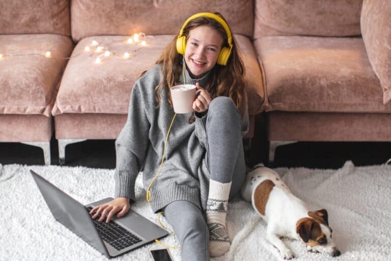 Teen girl wearing headphones by Christmas lights, dog, and computer