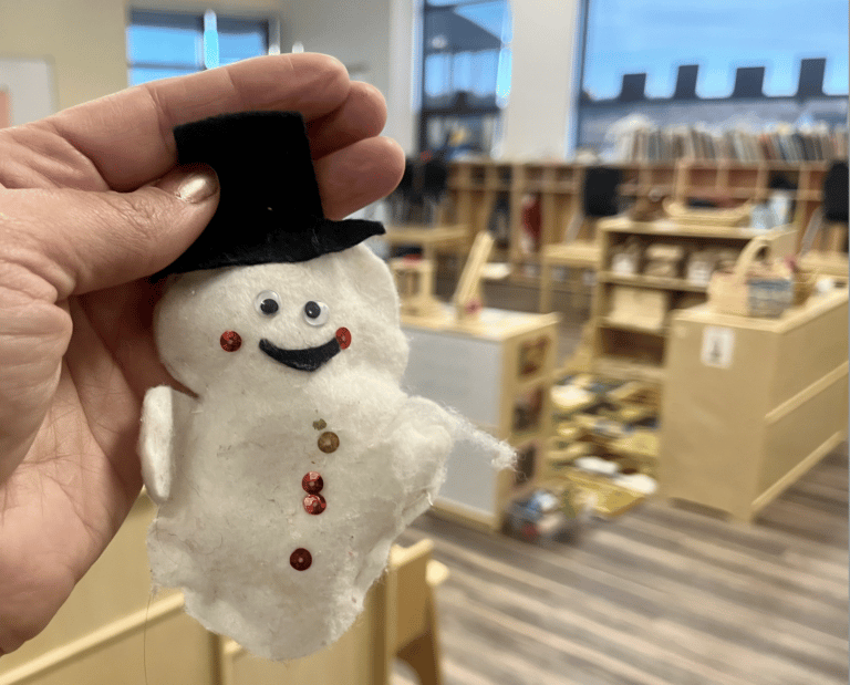 Child hanging handmade snowman ornament in classroom