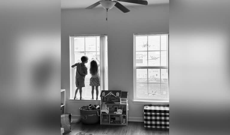 black and white photo of little boy and little girl standing in a window together