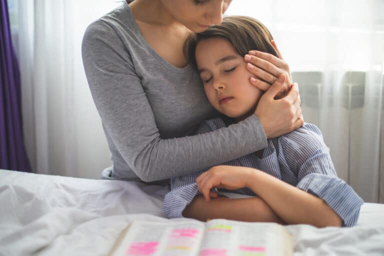 Mom hugging daughter by bed with open Bible