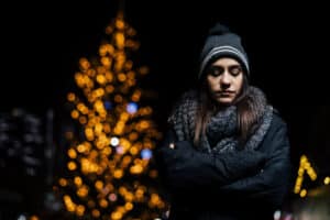Sad woman with Christmas tree lit up in background