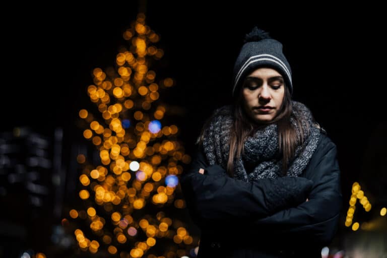 Sad woman with Christmas tree lit up in background