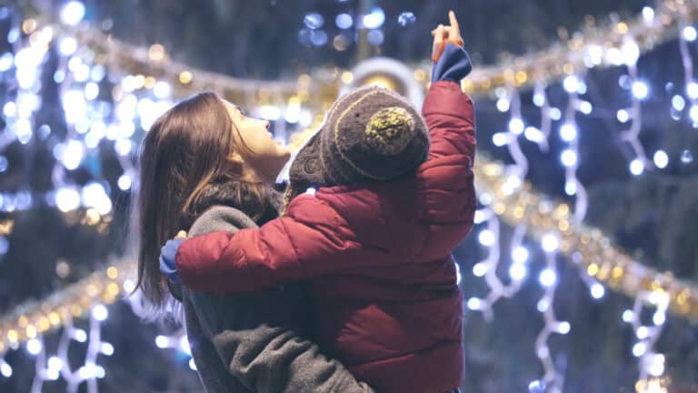 Mother holding child in front of Christmas lights