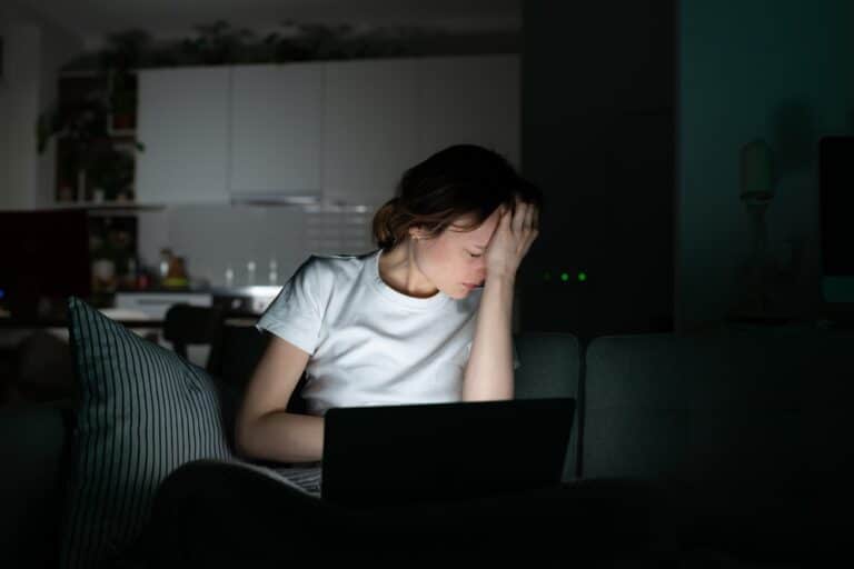 Tired woman holding forehead by light of computer in a dark room